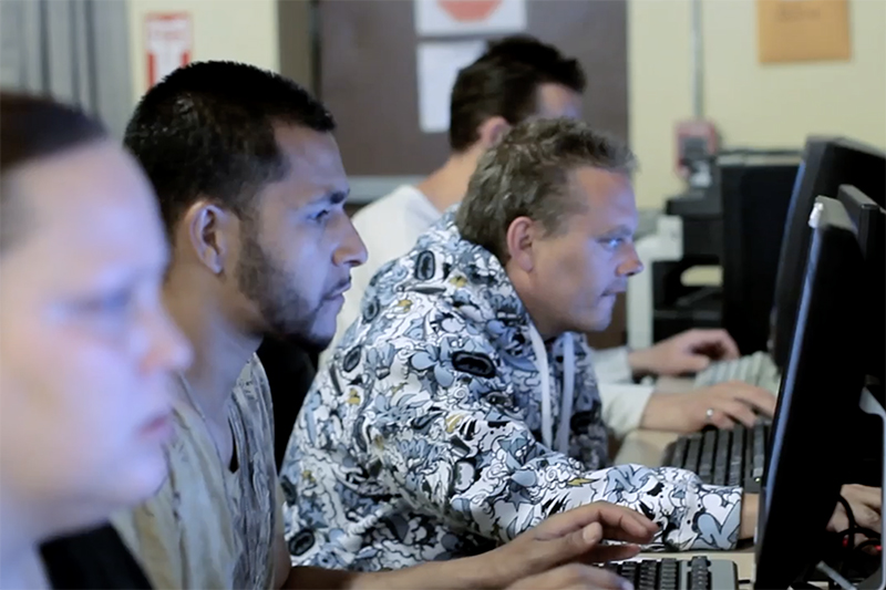 People sitting at a row of computer screens and keyboards